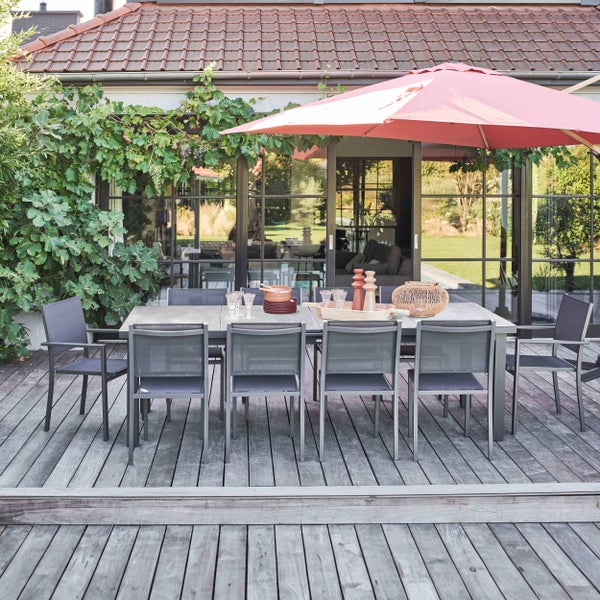 Modernes Garten-Essset mit grauem Tisch und acht Netzstühlen auf einer Holzterrasse unter einem roten Sonnenschirm.
