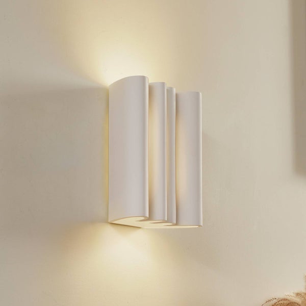 Moderne Wandleuchte in Weiß mit Wellen-Design und Up-and-Down-Lichteffekt an einer Wand montiert.