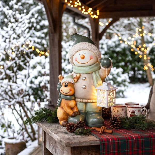 Dekorative Schneemann und Rentier Figur mit Laterne auf einem Holztisch mit winterlicher Dekoration im Hintergrund.