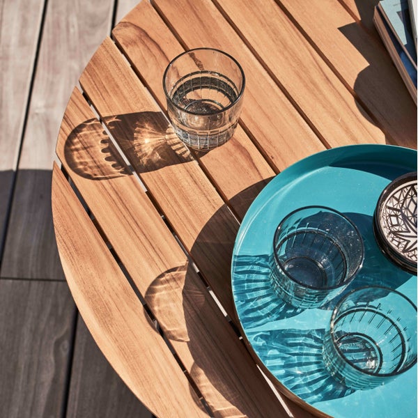 Runder Gartentisch aus Holzlatten mit Gläsern und einem Tablett in der Sonne.