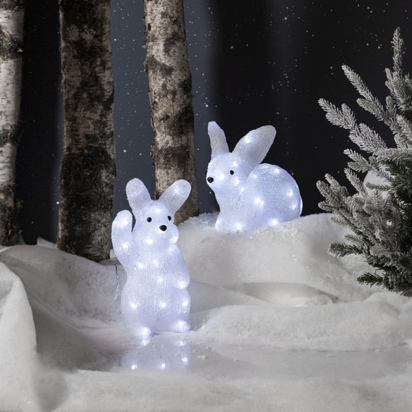 Szene mit zwei leuchtenden Hasenfiguren in einer verschneiten Winterlandschaft mit Birkenstämmen und einem kleinen Weihnachtsbaum