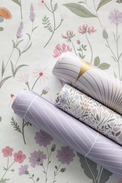 Drei Tapetenrollen mit unterschiedlichen Mustern auf einer floral gemusterten Oberfläche.
