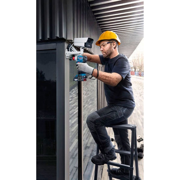 Ein Mann montiert auf einer Leiter stehend eine Überwachungskamera mit einem Akkuschrauber.