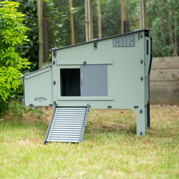 Erhöhter Hühnerstall Nestera aus recyceltem Kunststoff mit Rampe und offener Seitentür auf einem Rasen.
