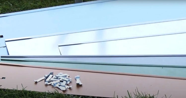 Mehrere farbige Metallplatten und Befestigungsklammern auf einer Rasenfläche.