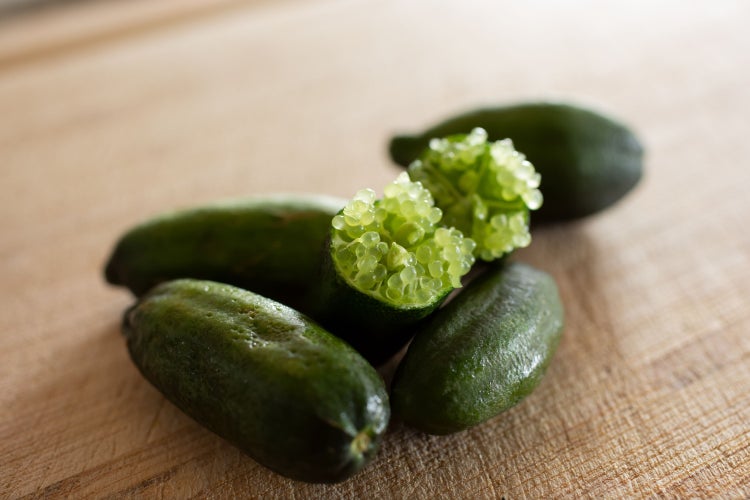 Aufgeschnittene grüne Fingerlimette mit perlenartigem Fruchtfleisch auf einer Holzoberfläche.