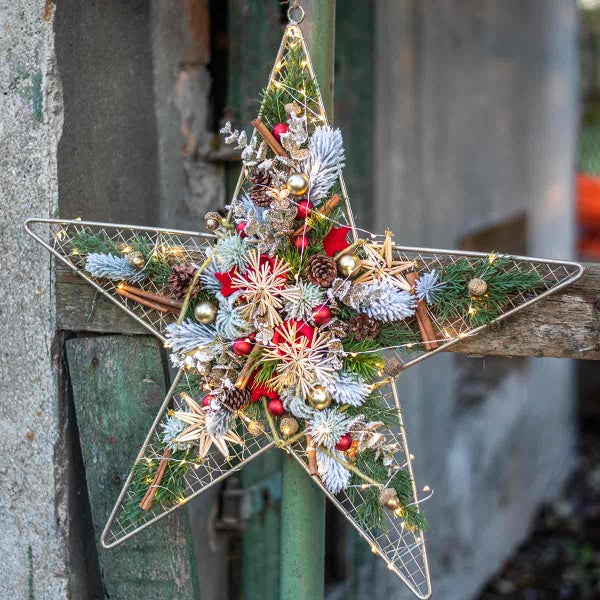 Weihnachtlicher Stern mit Dekoration aus Tannenzweigen, Kugeln, Zimtstangen und Lichtern als Weihnachtsschmuck