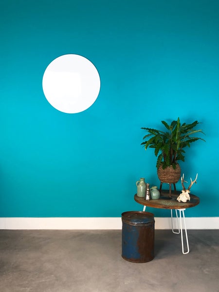 Innenraum mit türkis gestrichener Wand, runder Wanddekoration und Beistelltisch mit Pflanze und Dekoration.