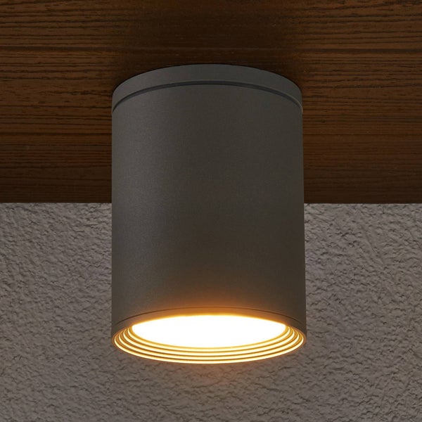 Zylindrischer Deckenaufbaustrahler aus Metall, montiert an einer Holzoberfläche, mit nach unten gerichtetem warmem Licht.