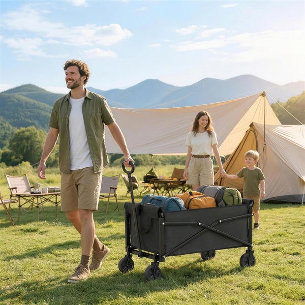 Eine Familie beim Camping auf einer Wiese, ein Mann zieht einen faltbaren Bollerwagen voller Gepäck vor einem Zelt bei sonnigem Wetter.