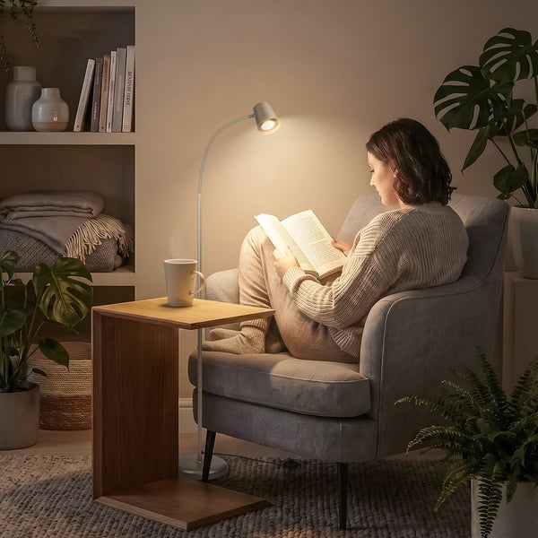 Eine Person sitzt in einem gemütlichen Sessel und liest ein Buch, beleuchtet durch eine schlichte Stehleuchte neben einem Beistelltisch aus Holz.