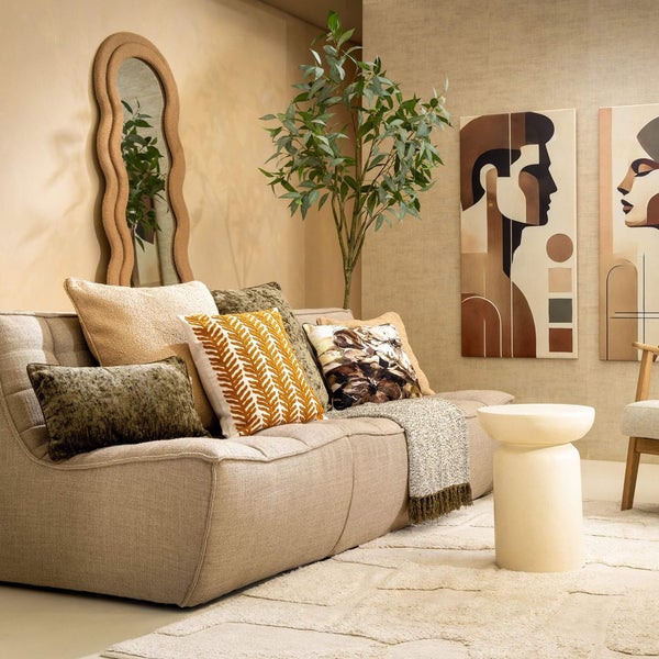 Wohnzimmer mit Sofa, Kissen, Spiegel, Beistelltisch, Teppich und Kunstwerken an der Wand.