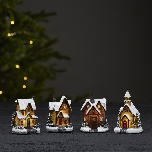 Vier dekorative Weihnachtshäuser mit Beleuchtung und Schnee vor einem Weihnachtsbaum