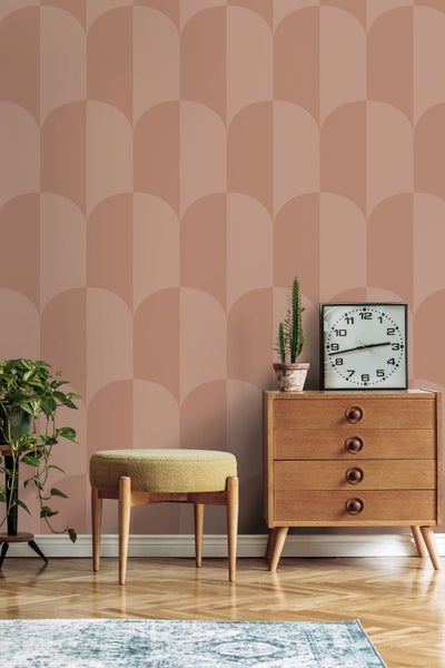 Vliestapete mit geometrischem Bogenmuster in einem Raum mit Holzkommode, runden Hocker und Zimmerpflanzen für ein modernes Wohnambiente.