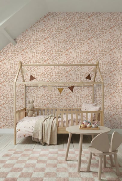 Helles Kinderzimmer mit floraler Vliestapete an der Wand, einem Hausbett aus Holz, rundem Kindertisch und gemustertem Teppich.
