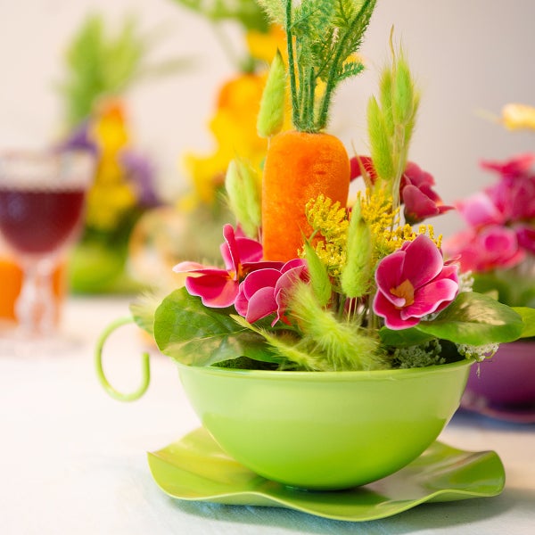 Dekoration mit Kunstblumen und Karotte in einer grünen Tasse