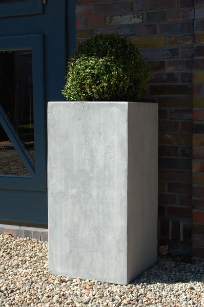 Hoher, rechteckiger Pflanzkübel aus grauem Beton mit einer Buchsbaumkugel vor einer Ziegelwand im Außenbereich.