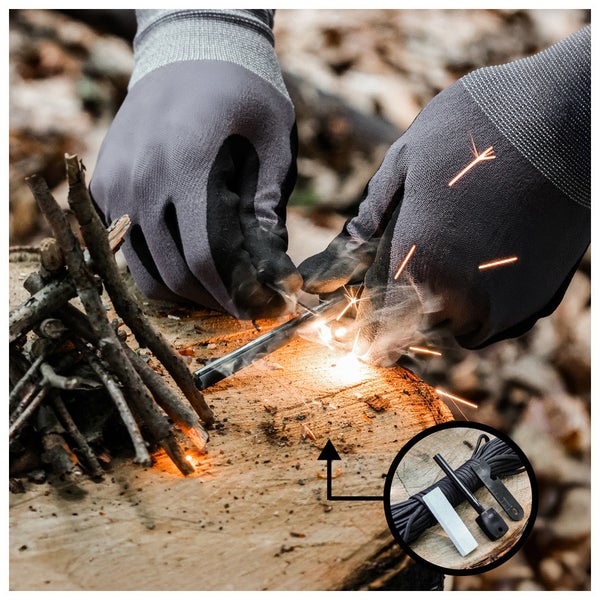 Zwei Hände mit Arbeitshandschuhen entzünden ein Feuer mit einem Feuerstarter neben einem Stapel Holz auf einem Baumstumpf.