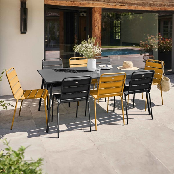 Moderne Garten-Sitzgruppe mit rechteckigem Tisch in Dunkelgrau und gelben sowie grauen Metallstühlen auf einer hellen Steinterrasse.