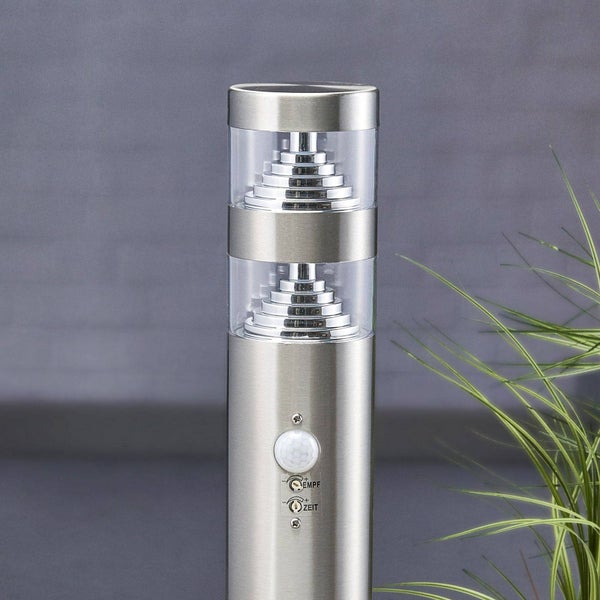 Zylindrische Außenleuchte aus Edelstahl mit zwei klaren Lichtauslässen, Bewegungsmelder und Einstellreglern für Empfindlichkeit und Zeit.