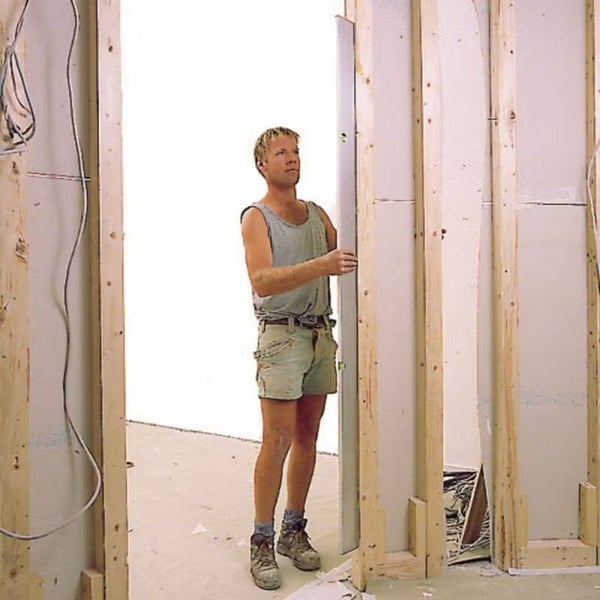 Handwerker überprüft die vertikale Ausrichtung eines Holzständerwerks für eine Trockenbauwand mit einer langen Wasserwaage.