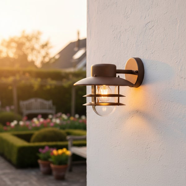 Außenwandleuchte im modernen industriellen Design mit einem klaren Leuchtmittel, montiert an einer weißen Wand vor einem Gartenhintergrund.