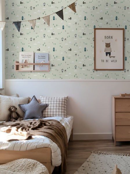 Kinderzimmer mit Vliestapete im Muster aus kleinen Häusern und Bäumen, ausgestattet mit Holzmöbeln und Textilien.