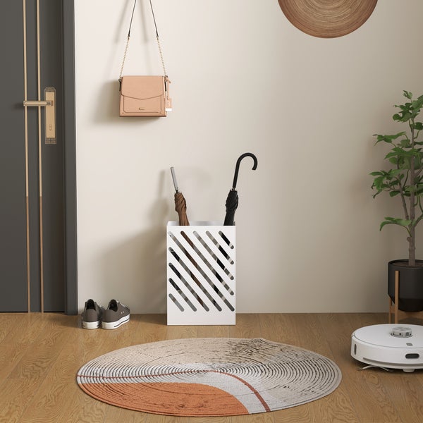 Moderner weißer Regenschirmständer aus Metall mit diagonalen Schlitzen in einem hellen Eingangsbereich neben einer Tür.