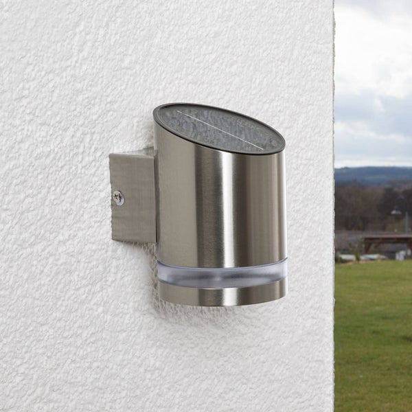 Solar-Wandleuchte aus Edelstahl, zylinderförmig mit schräger Oberseite und integriertem Solarpanel, montiert an einer Außenwand.