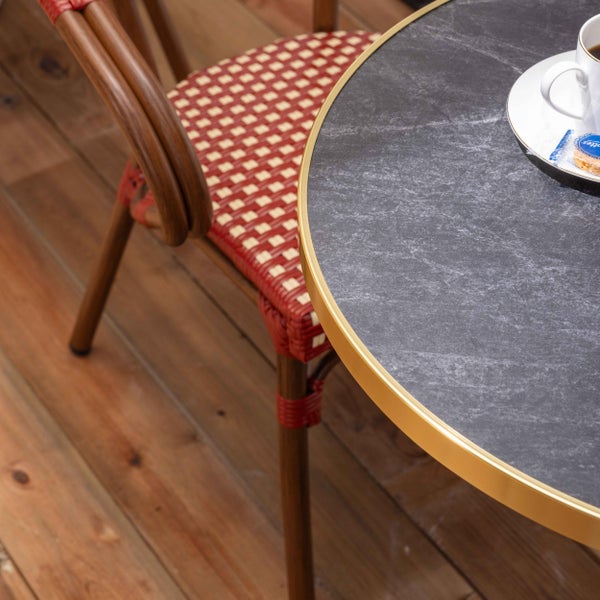 Runder Bistrotisch mit Marmor-Optik und Goldrand sowie ein geflochtener Bistrostuhl auf einer Holzterrasse.
