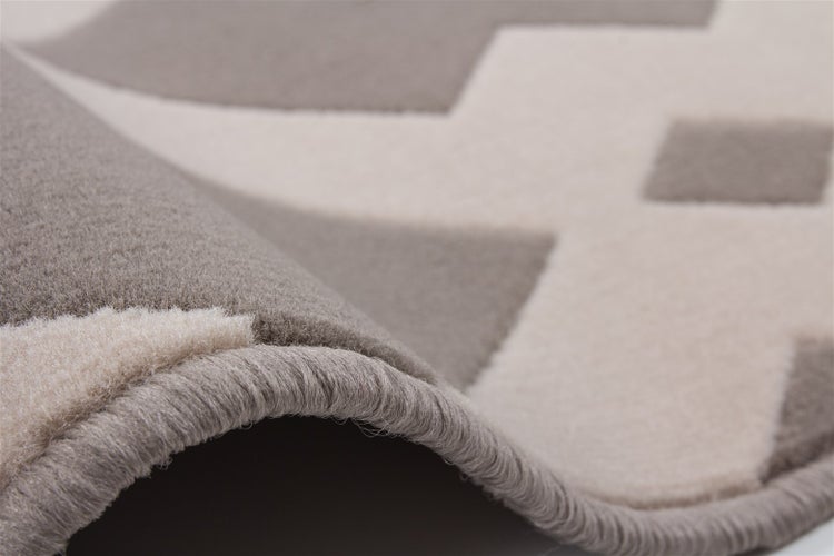Detailaufnahme eines Teppichs mit geometrischem Muster, die den gefalteten Rand und die Textur des Flors zeigt.