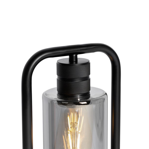 Detailansicht einer Tischleuchte mit schwarzem Metallbügel, zylindrischem Rauchglas und leuchtendem Filament-Leuchtmittel.
