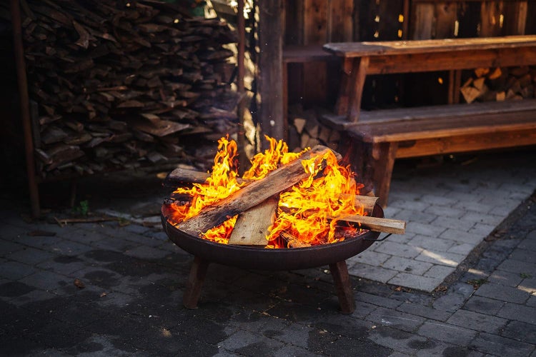 Szene mit brennendem Lagerfeuer in einer Feuerschale, im Hintergrund Menschen und ein See