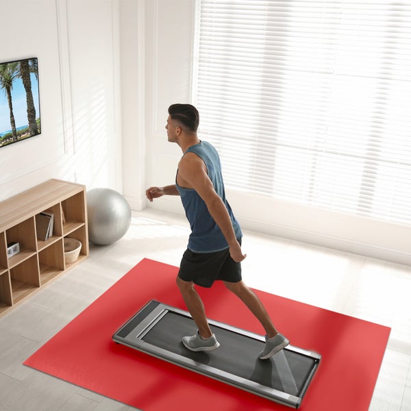 Ein Mann trainiert auf einem Laufband auf einer orangefarbenen Bodenschutzmatte in einem hellen, modern eingerichteten Zimmer.