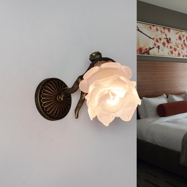 Wandleuchte mit Blumenmuster neben einem Bett.