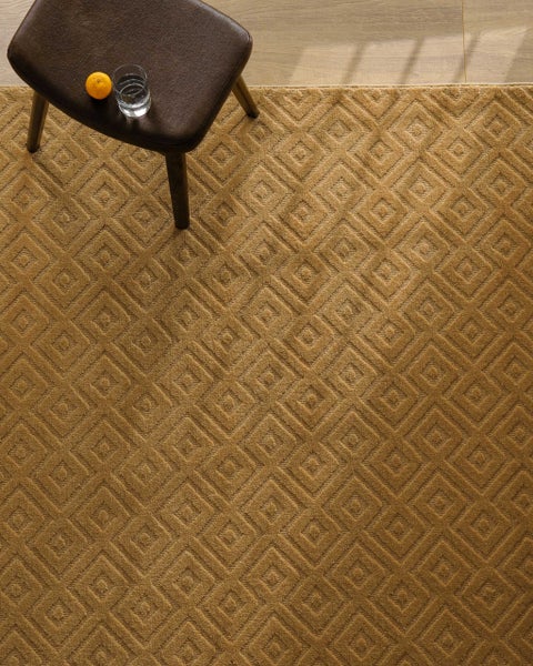 Nahaufnahme eines weichen, strukturierten Teppichs mit geometrischem Quadratmuster auf einem Boden in Holzoptik.