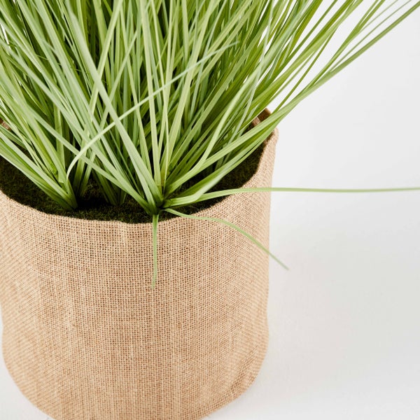 Künstliches Ziergras in einem Topf mit Jute-Ummantelung.