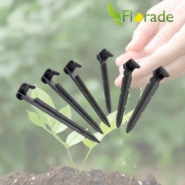 Hand hält Kunststoff Erdnägel für Bewässerungsschläuche vor einem Pflanzenhintergrund mit Florade Logo