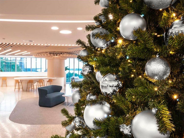 Ein geschmückter Weihnachtsbaum mit silbernen Christbaumkugeln und Lichterkette in einem modernen, hellen Büro-Ambiente.