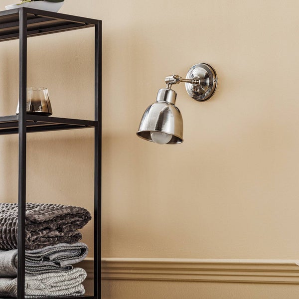 Wandleuchte aus Metall neben einem Regal mit Textilien und Glas