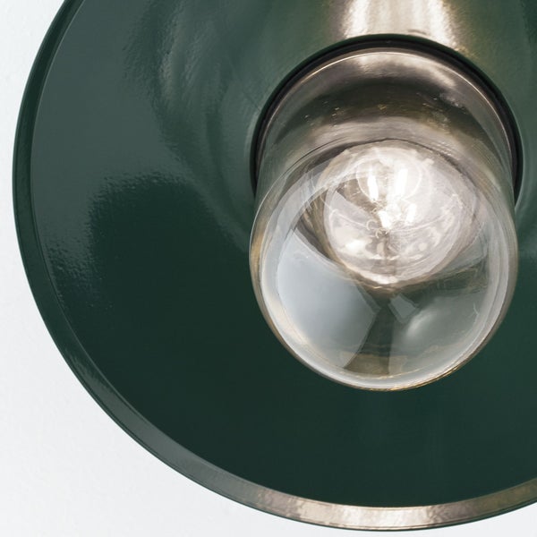Nahaufnahme einer Lampe mit einem dunkelgrünen Metallschirm und einer klaren Glasabdeckung über dem Leuchtmittel.