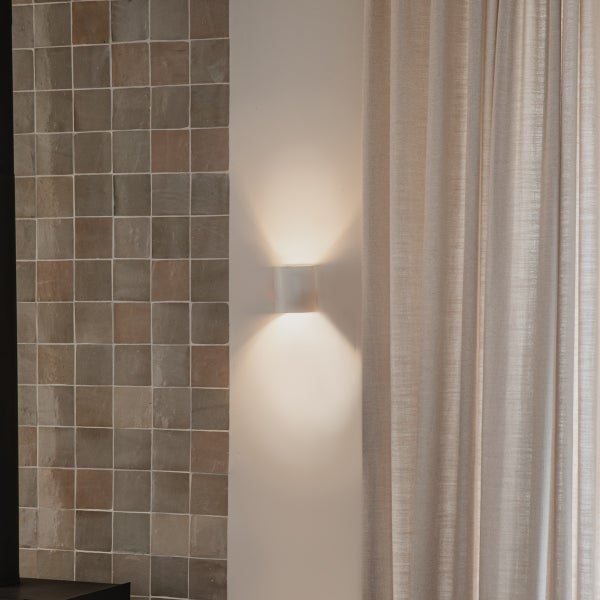 Wandleuchte neben Fliesenwand und Gardine