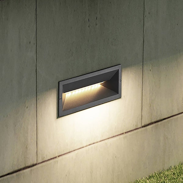 Rechteckige LED-Wandeinbauleuchte aus anthrazitfarbenem Metall in einer Betonwand mit warmweißem Lichtschein.