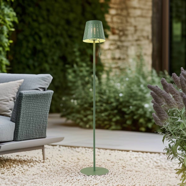 Grüne Stehleuchte für den Außenbereich mit gelochtem Schirm auf einer Terrasse mit Kies und Gartenmöbeln.