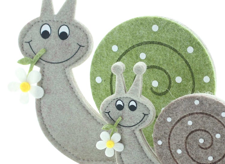 Dekorative Schneckenfiguren aus Filz auf Holzsockel, jeweils mit einer kleinen Blume im Mund.