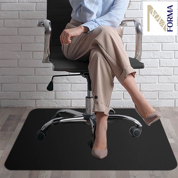 Schwarze Bodenschutzmatte unter einem Bürostuhl auf Holzboden in einem hellen Raum mit Ziegelwand. NOVA FORMA Logo.