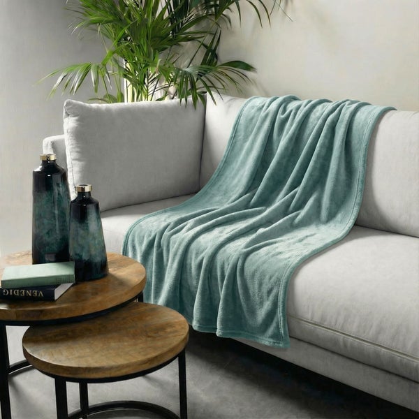 Wohnszene mit Sofa, türkisfarbener Kuscheldecke und Dekorationselementen