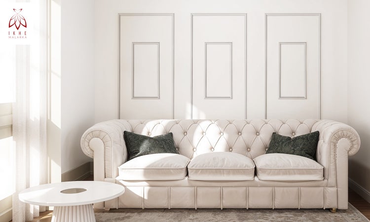 Helles Wohnzimmer mit hellem Dreisitzer-Chesterfield-Sofa, dunkelgrünen Kissen und Wandleisten. Ikhe Malarka Logo.