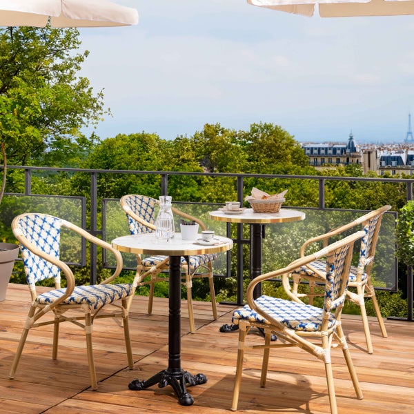 Bistro-Set auf Holzterrasse mit Stadtblick, zwei runde Marmortische und vier blau-weiß geflochtene Stühle im französischen Stil.