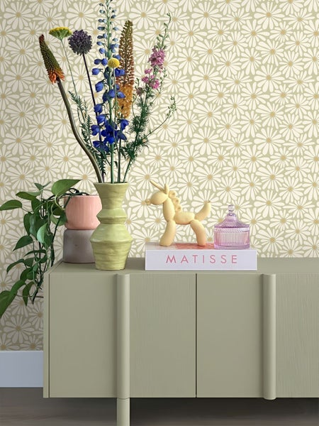 Helle Raumszene mit Tapete mit Gänseblümchen-Muster, einem hellgrünen Sideboard, einer Vase mit bunten Blumen und Dekoartikeln.